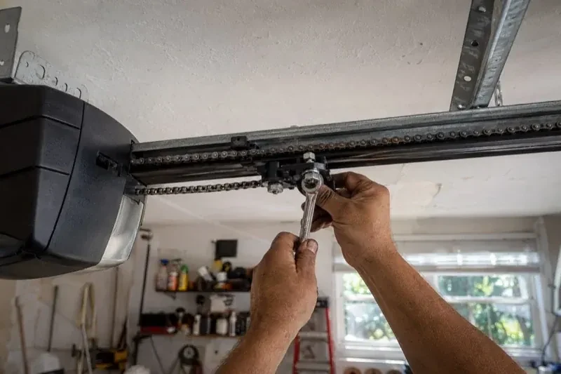 Hands holding a wrench against an opener trolley beneath a chain rail — Chain-Drive Opener Repair, Centre Wellington