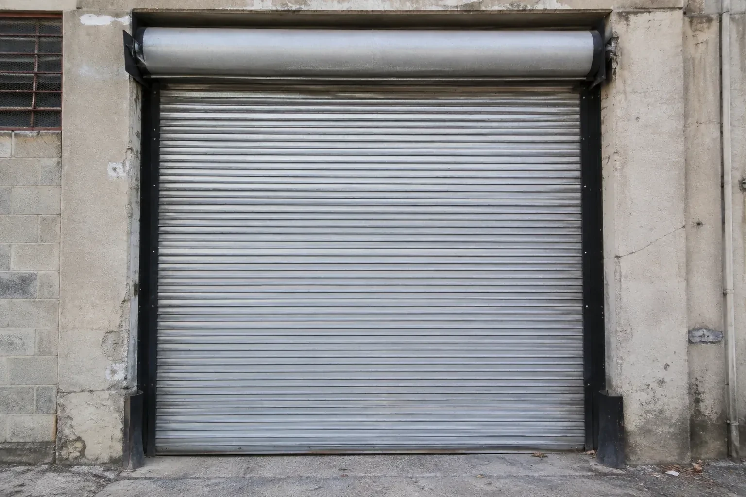 Closed metal rolling shutter in a weathered warehouse opening. — Commercial Rolling Door Repair, Centre Wellington