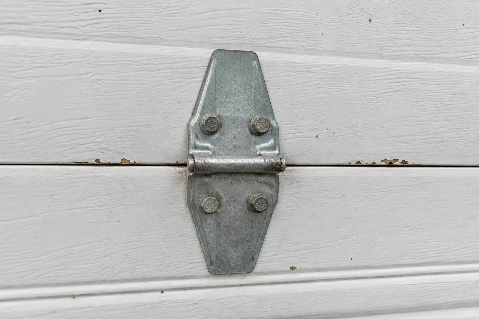 Metal center hinge across a seam in a white sectional garage door. — Garage Door Hinge Replacement, Centre Wellington