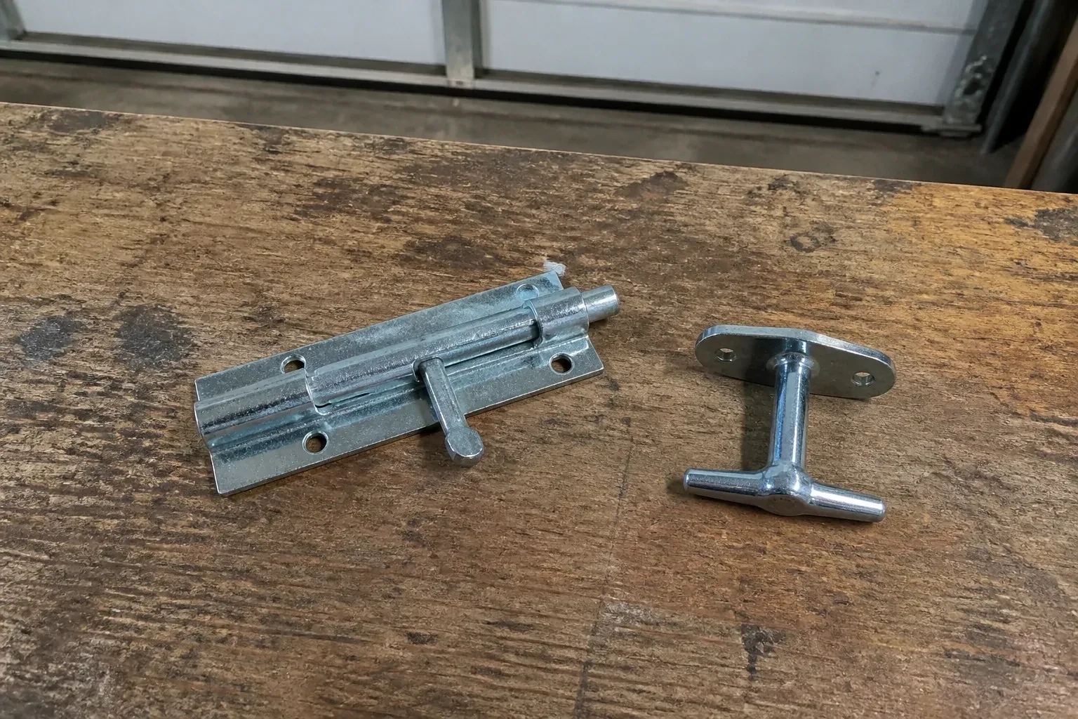 Detached slide bolt and T-handle on a wooden garage workbench. — Garage Door Manual Lock Repair, Centre Wellington