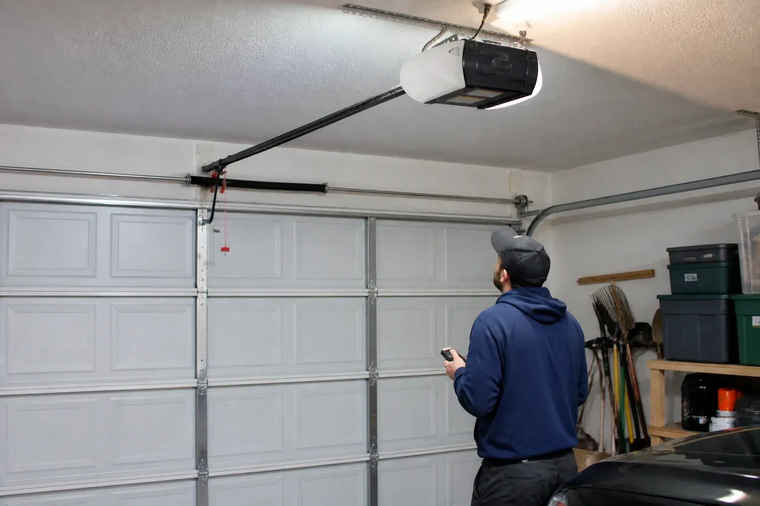A person holding a remote looks toward an overhead garage-door opener and rail. — Garage Door Opener Diagnosis and Repair, Centre Wellington
