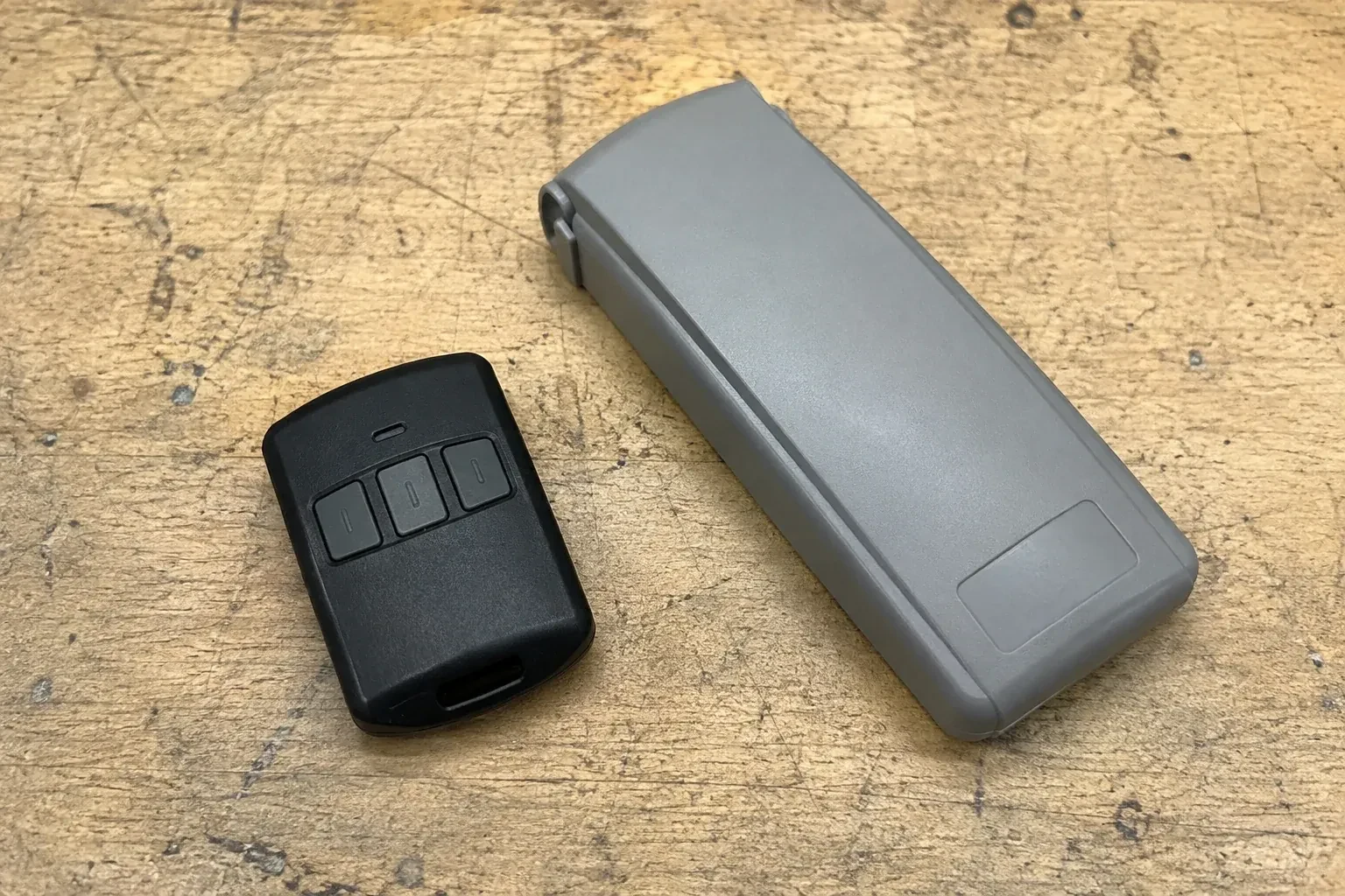 Three-button remote beside a closed grey keypad cover on a workbench. — Garage Door Remote and Keypad Programming, Centre Wellington
