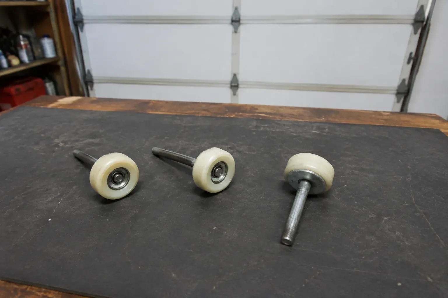 Three detached nylon-wheel garage door rollers with steel stems on a work mat. — Garage Door Roller Replacement, Centre Wellington