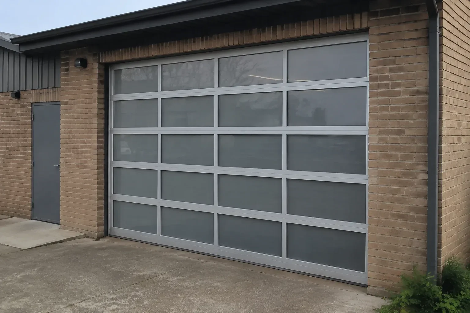 Closed glazed sectional door in a grey metal frame at a brick workshop. — Full-View Glass Garage Door Installation, Centre Wellington